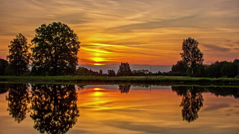 Vibrant-sunrise-with-the-golden-sky-reflecting-off-the-surface-of-a-lake---time-lapse