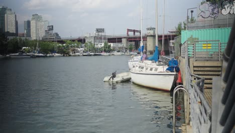 Ein-älteres-Weißes-Segelboot-Mit-Einem-Einzigen-Rumpf-Und-Einem-Daneben-Geparkten-Beiboot-Ruht-Zufrieden-An-Der-Kanalwand-In-Greenpoint,-Brooklyn