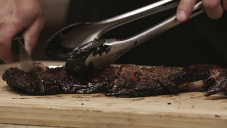 Close-up-on-BBQ-pork-ribs-being-cut-with-a-knife-and-tongs-on-cutting-board