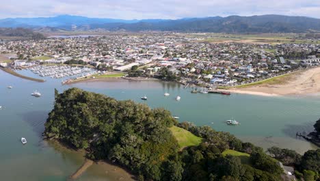 Aerial-pull-back-of-Whitianga,-small-town-on-beachfront,-marine-port,-beach-and-townscape
