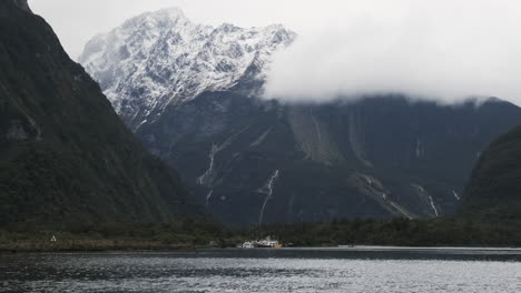 Boats-anchored-in-front-of-massive-snow-covered-cliff,-Milford-Sound,-New-Zealand