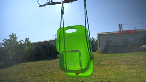 Aufsteigende-Aufnahme-Einer-Kaputten-Grünen-Plastikschaukel-In-Einem-Sonnigen-Garten-In-Frankreich-In-Zeitlupe-Für-Kinder-Unter-Einem-Wolkenlosen-Himmel