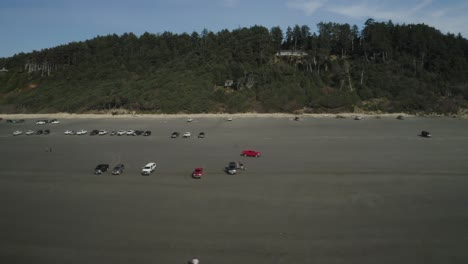 Red-Car-Driving-Through-Parked-Vehicles-On-Sandy-Beach-Of-Iron-Springs-Resort-In-Ocean-Shores,-Washington,-USA