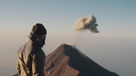 Hiker-On-Top-Of-Acatenango-Volcano-Summit-Looking-At-Fuego-Volcano-Eruption-In-Guatemala,-Central-America