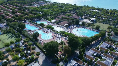 Large-swimming-pools-full-of-people-on-holiday-or-vacation-near-Lake-Garda-Italy,-aerial-parallax