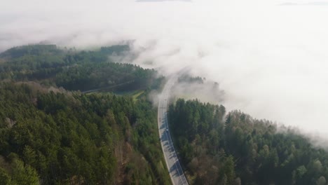 Aerial-view-of-a-road-leading-into-the-fog-with-cars-passing-by-on-a-spring-morning