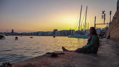 Young-female-tourist-sitting-as-the-sunsets-over-Sliema,-Malta---time-lapse