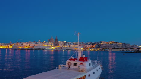 Twilight-to-nighttime-time-lapse-of-Valletta,-Malta-with-a-boat-in-the-foreground---time-lapse