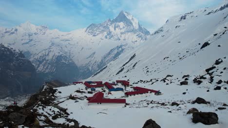 Cinematic-Aerial-View-Of-Annapurna-Base-Camp-On-Snow-Covered-Mountain-Side-With-Machapuchare-Peak-In-Background