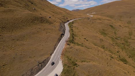 Dark-car-driving-down-winding-mountain-pass-road-on-sunny-day-in-southern-New-Zealand