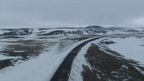 Seguimiento-De-La-Toma-De-Drones-De-Un-Automóvil-Que-Se-Mueve-En-Una-Carretera-Vacía-En-El-Desierto-De-Islandia-A-Fines-De-La-Temporada-De-Invierno