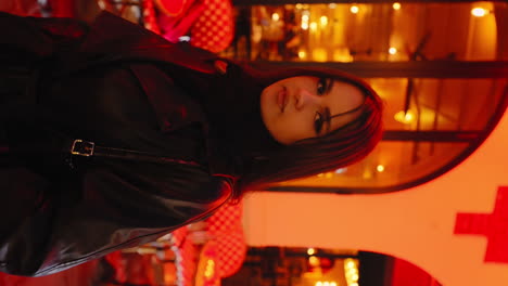 Vertical-video-of-a-beautiful-young-woman-looking-at-the-camera,-in-front-of-a-restaurant,-in-Paris-near-Montmartre,-at-night