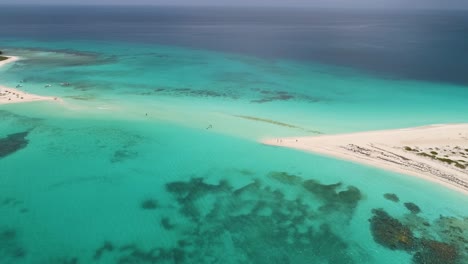 PEOPLE-walk-flooded-sandbank-CAYO-DE-AGUA-ISLAND-ON-SHALLOW-WATER,-AERIAL-VIEW-TURQUOISE-WATER-TEXTURE-AND-CORAL-REEF
