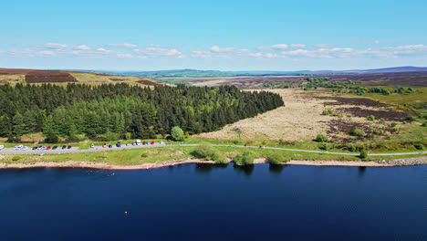 The-picturesque-Winscar-Reservoir-in-Yorkshire-sets-the-stage-for-a-dazzling-boat-race,-as-small-one-man-boats-with-white-sails-compete-in-the-serene-blue-lake,-basking-in-the-radiant-midday-sunlight