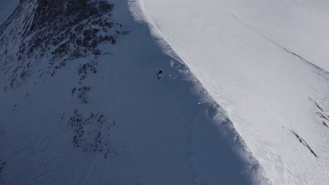 Aerial-top-down-shot-of-lonely-Skier-Carving-down-extremely-steep-snowy-and-rocky-mountain-during-sun