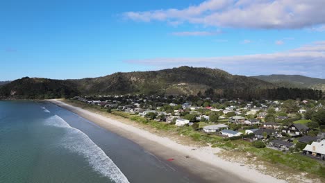 Houses-on-Matarangi-beachfront,-sandy-beach,-forested-hills
