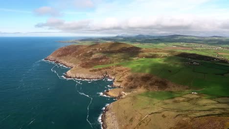 Aerial-panoramic-view-of-waves-crashing-on-the-cliffs-on-the-tip-of-the-Llyn-Peninsula-at-Uwchmynydd,-a-dramatic-coastline-with-shadows-of-clouds-over-the-vast-landscape-on-a-sunny-day-in-North-Wales
