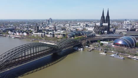 Cologne-Cathedral,-musical-Dome-and-Railway-Bridge-in-a-Riverscape-aerial-of-Cologne-city,-Germany