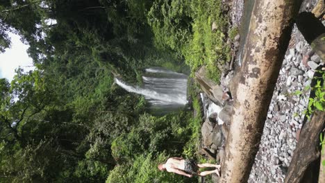 Vertical-format:-Tourist-man-walks-on-log-below-Tiu-Kelep-waterfall