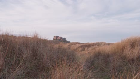 Ground-level-fixed-shot-of-Bamburgh-castle-in-the-distance,-with-tall-grassy-sand-dunes-in-the-foreground