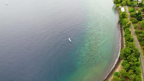Aerial-drone-of-traditional-Indonesian-wooden-fishing-boat-in-crystal-clear-ocean-water-along-beautiful-coastline-of-Alor-Island,-East-Nusa-Tenggara,-Indonesia