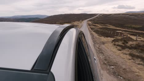 Adventurous,-scenic-drive-through-the-majestic-Scottish-Highlands-in-a-silver-SUV,-with-a-captivating-view-towards-the-long-road-stretching-through-the-vast-brown-landscape-in-the-back