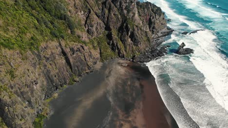 Luftaufnahme-Eines-Klaren,-Unverschmutzten-Paradiesischen-Strandes-Mit-Wellen,-Die-Auf-Die-Felsklippe-Stürzen,-Comans-Track,-Karekare,-Neuseeland