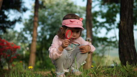 Curious-young-toddler-squatting-examines-dandelion-with-magnifying-glass