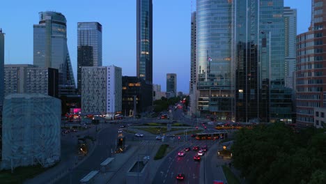 Aerial-view-of-Warsaw-during-the-captivating-blue-hour,-with-the-modern-office-buildings-of-Rondo-ONZ-reflecting-the-vibrant-city-traffic-below