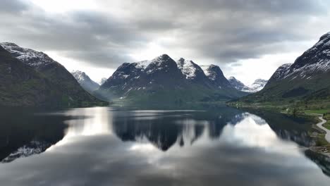 Rising-morning-aerial-above-Oppstrynsvatnet-lake-with-stunning-mountain-landscape-background-and-surays-penetrating-through-valley-on-the-left---Mounain-reflections-in-water-surface