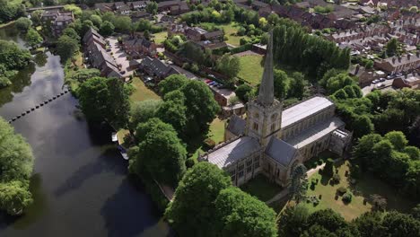 Establishing-aerial-view-looking-down-over-lush-green-Warwickshire-countryside,-river-Avon-and-quaint-Holy-Trinity-church