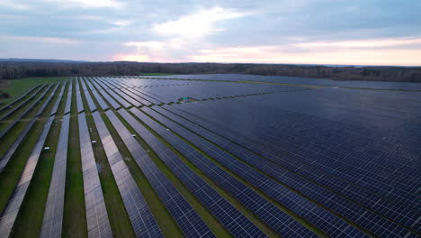 Vast-solar-farm-with-long-rows-of-solar-PV-panels,-aerial-pullback-view
