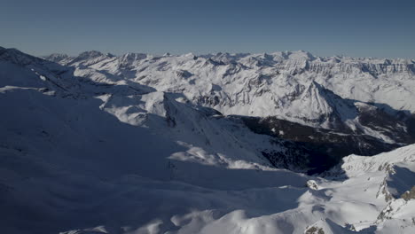 Eine-Nach-Unten-Geneigte-Luftaufnahme-Zeigt-Eine-Wunderschöne-Verschneite-Berglandschaft-Und-Ein-Tal-An-Einem-Sonnigen-Tag-Mit-Blauem-Himmel-In-Österreich