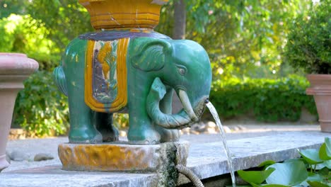 Slow-revealing-shot-of-a-green-and-gold-cultural-elephant-water-fountain-in-a-garden