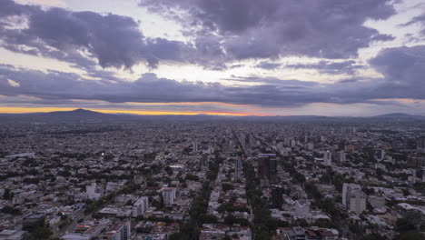 Hyperlapse-featuring-a-sunrise-over-the-expansive-metropolitan-area-of-Guadalajara,-highlighting-its-impressive-infrastructure-and-beautiful-reddish-clouds-as-the-sun-rises