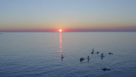 Gruppe-Von-Paddle-Boardern-Auf-Dem-Wasser-Bei-Sonnenuntergang,-Die-Den-Sonnenuntergang-Unter-Dem-Horizont-Beobachten