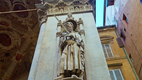 A-statue-adorns-a-pillar-of-the-Merchants-Lodge,-Loggia-della-Mercanzia-located-behind-the-Piazza-del-Campo,-in-Siena,-Italy