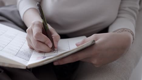 Close-up-of-woman-writing-in-her-schedule-planner,-using-pencil-and-white-paper-book,-calendar-and-planning-management-concept
