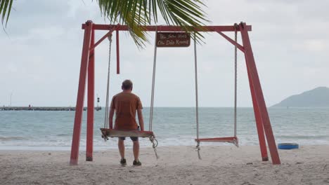 Man-Sitting-On-A-Swing-Enjoying-The-View-Of-The-An-Hai-Beach-From-Sandy-Shore-In-Con-Dao,-Vietnam
