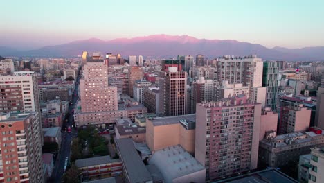 Die-Innenstadt-Von-Santiago-Kontrastiert-Alte-Und-Moderne-Wolkenkratzergebäude-Im-Stadtbild-Mit-Der-Luftaufnahme-Der-Skyline-Der-Anden-Bei-Sonnenuntergang