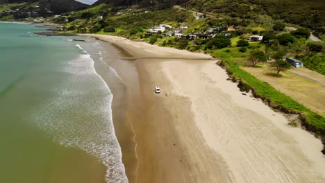 White-van-driving-on-sandy-beach-at-Shipwreck-Bay,-Ahipara,-New-Zealand