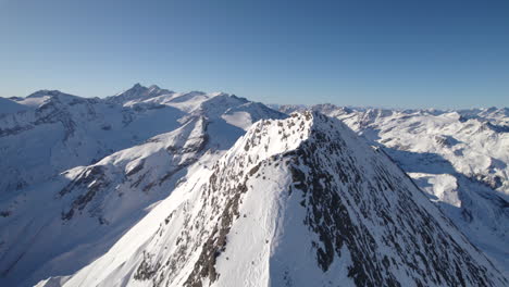 Drone-flying-around-top-of-mountain-with-snowy-landscape-in-background-on-sunny-day-in-Austria
