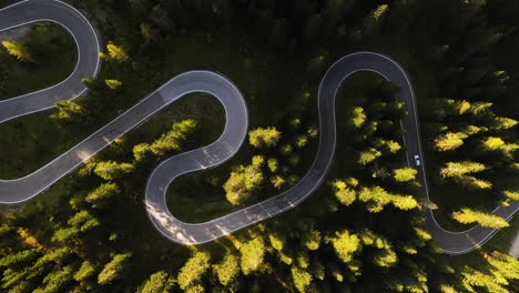 Aerial-overview-of-a-car-on-a-winding-road,-golden-hour-in-Dolomites,-Italy---birds-eye,-drone-shot