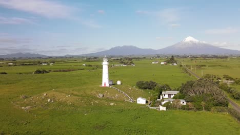 Wunderschöner-Malerischer-Ort-Des-Leuchtturms-Von-Cape-Egmont-Und-Des-Majestätischen-Kegelförmigen-Vulkans-Taranaki-Am-Horizont---Drohnenumlaufbahn