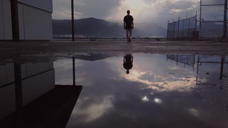 Reflection-Of-A-Young-Man-In-The-Puddle,-Whilst-Walking-And-Appreciating-The-Skies-That-Shining-Through-The-Mountains---low-angle
