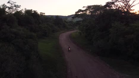 Motorbike-riders-cruise-down-dusty-dirt-road-high-in-mountains-at-sunset