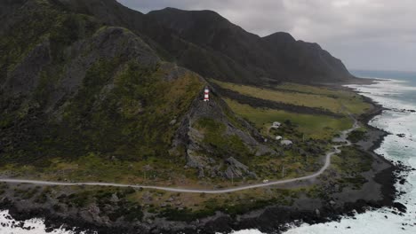Iconic-Cape-Palliser-Lighthouse-aerial-pull-back,-dramatic-cloudy-day