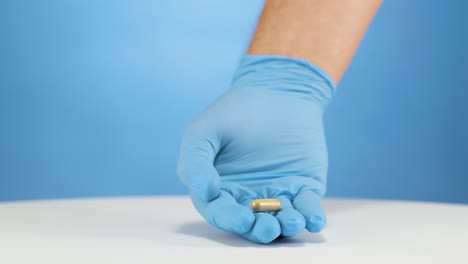 Caucasian-hand-with-blue-gloves-establishes-light-brown-capsule,-concept-of-pain