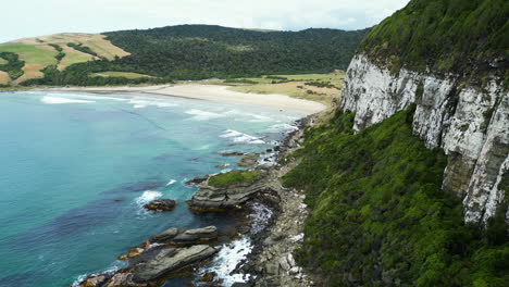 Aerial-view-of-cliff-revealing-paradise-beach-at-Parakaunui-bay,-New-Zealand