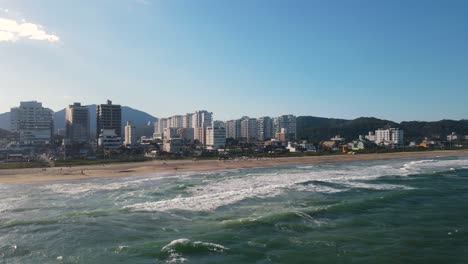 Drone-shot-of-praia-brava-in-Brazil-with-the-sea-and-buildings-on-the-background